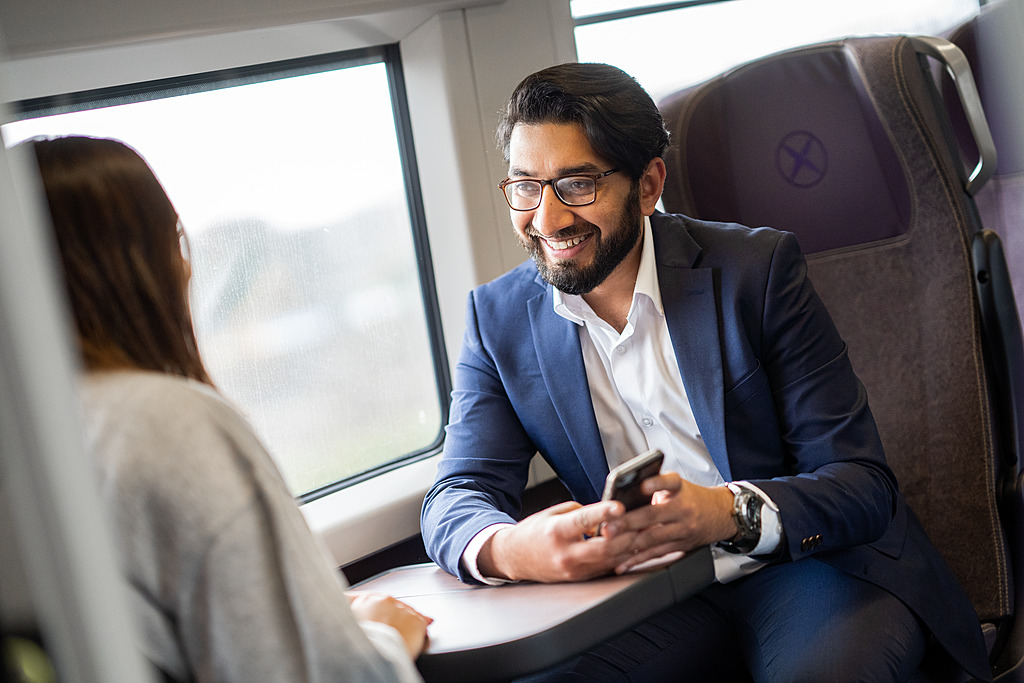 A map smiling on the Heathrow Express with his phone out